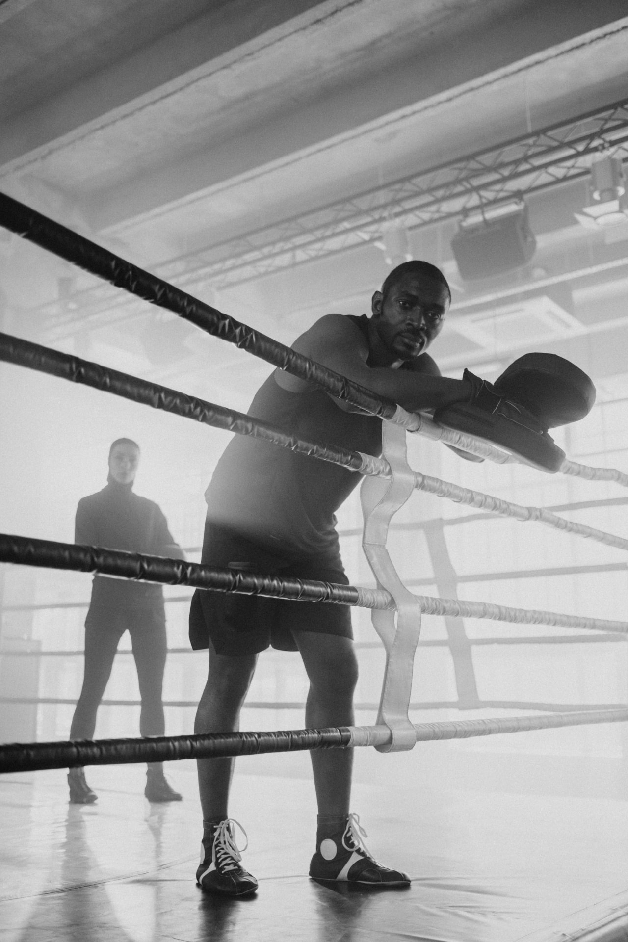 A fighter leaning on the ring ropes with pad gloves after a round