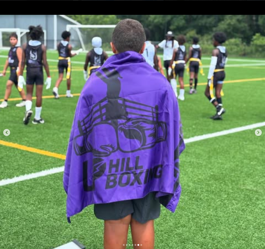A young player wearing the purple UpHill Boxing team banner on a flag football field